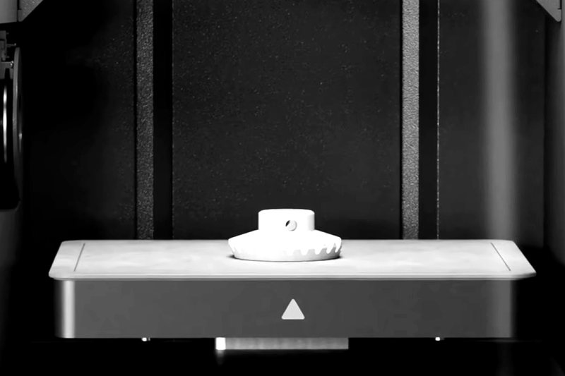 Metal additively manufactured bevel gear with hub and cross-hole on the build plate.