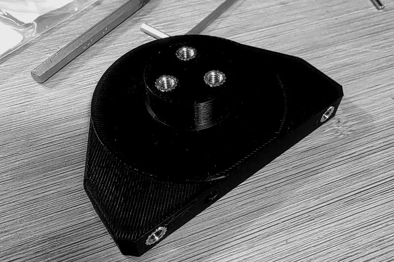 Black additively manufactured mount with a raised boss and heat-set brass threaded inserts.