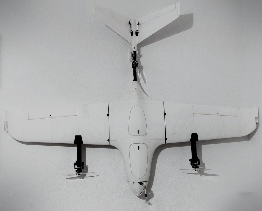 White VTOL fixed-wing UAV R&D platform with V-tail, pusher propeller and two vertical-lift rotor booms, seen from above.
