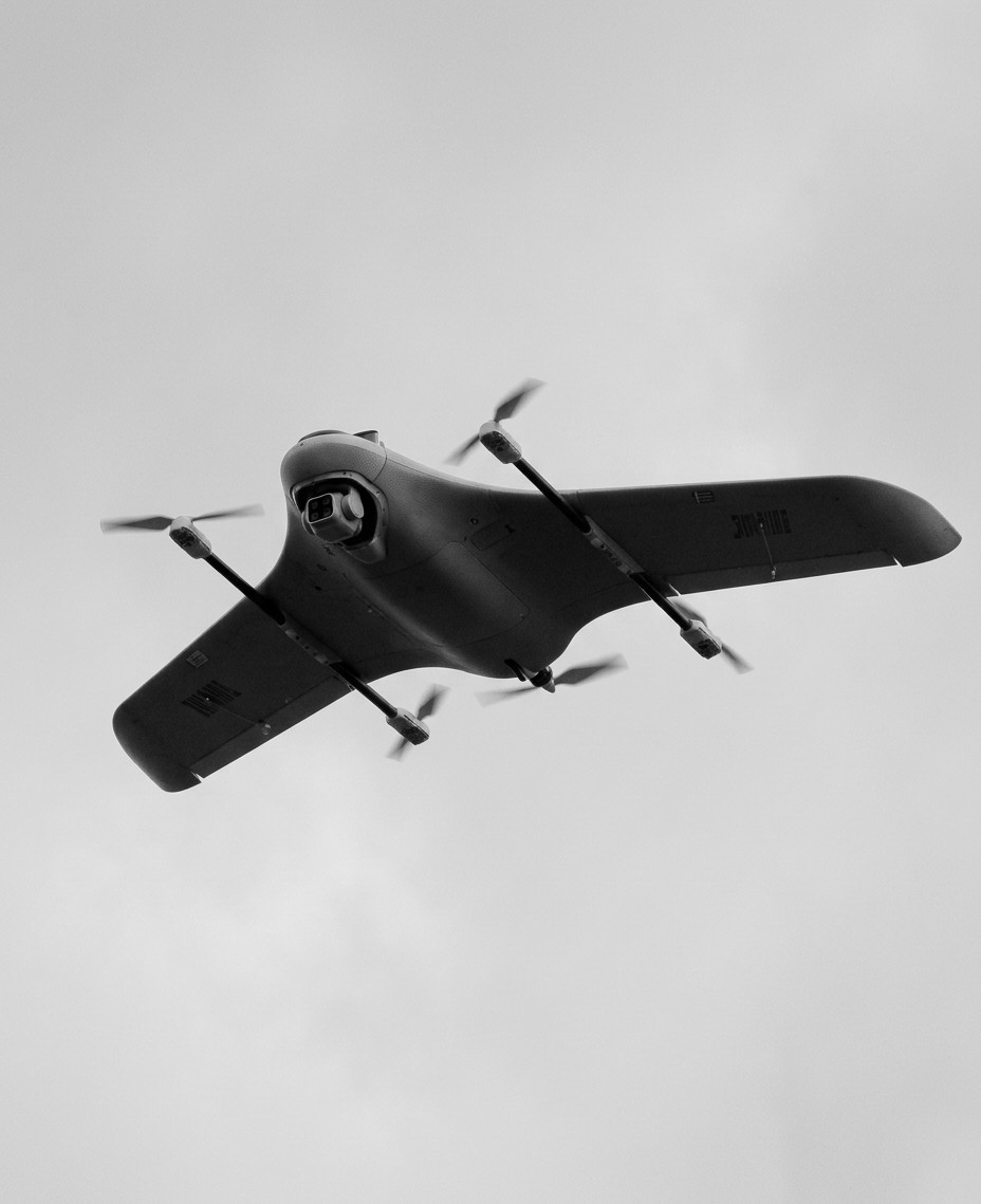 VTOL flying-wing UAV R&D platform in flight, seen from below, with four lift rotors on two booms.